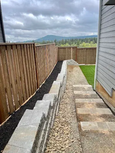Block retaining wall stepping down a side yard beside a fence