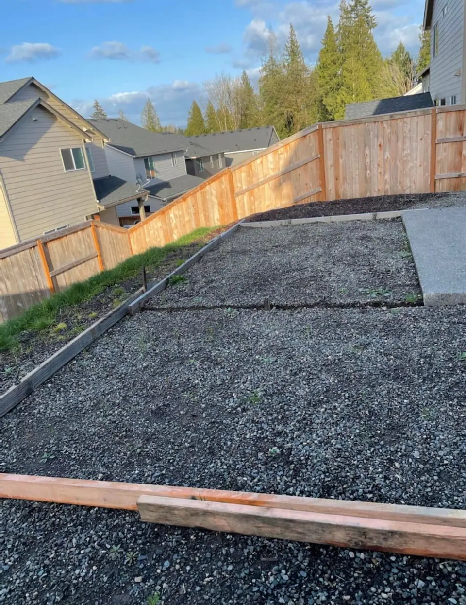 Compacted gravel base prepared across a fenced backyard before hardscape installation
