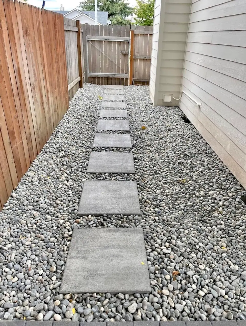 Concrete stepping stones in river rock along a narrow side yard