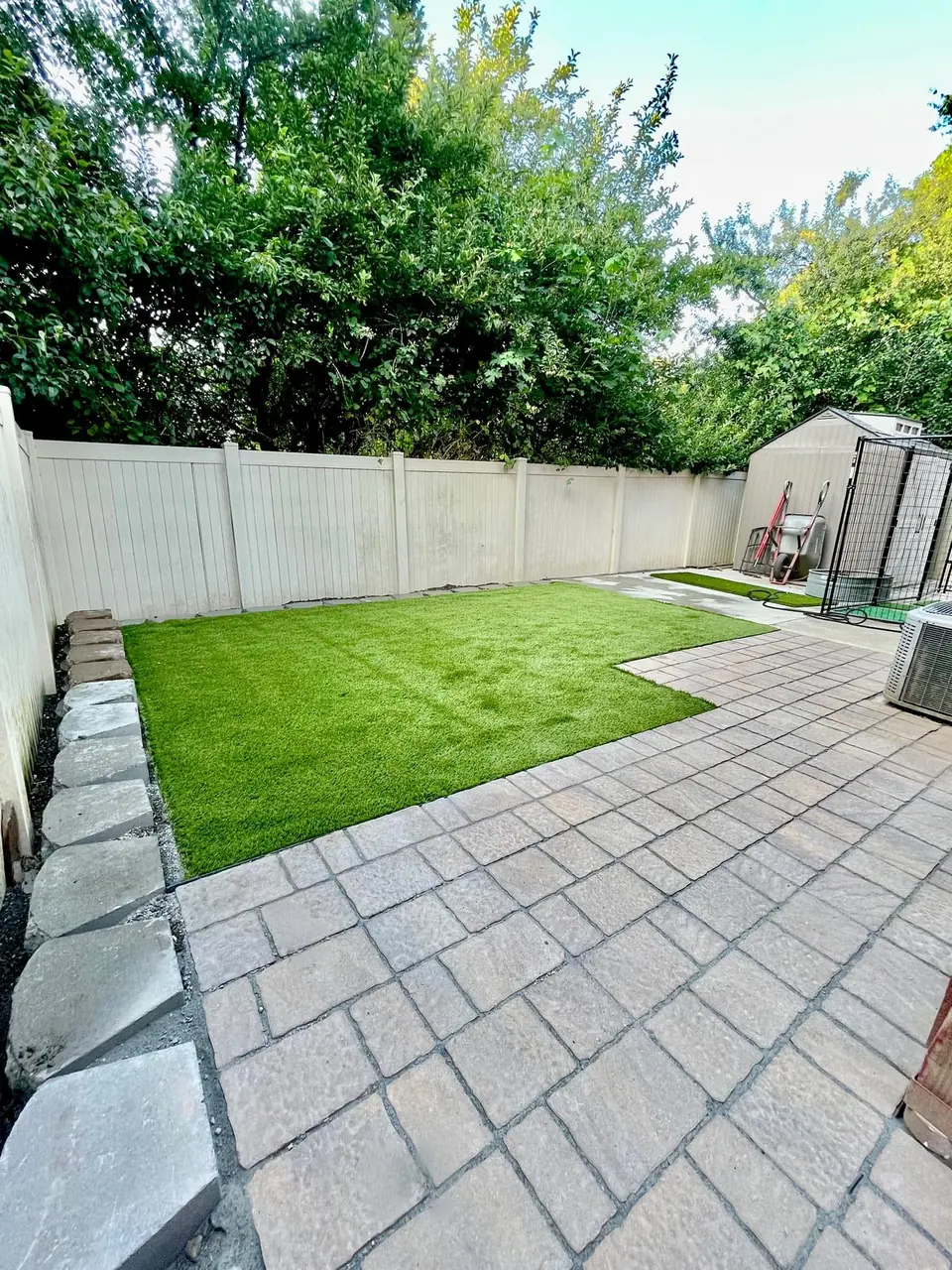 Paver patio and lawn finished behind a white vinyl fence