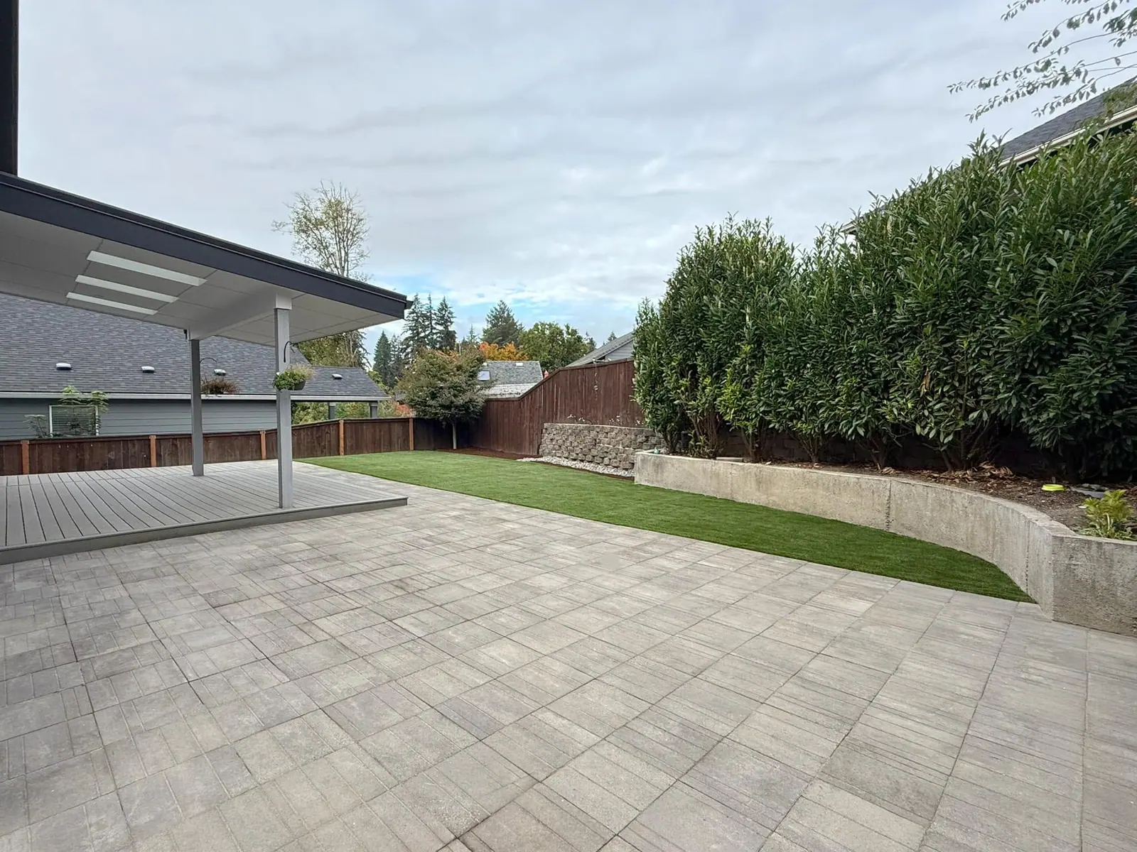 Paver patio bordered by a block wall and mature hedge