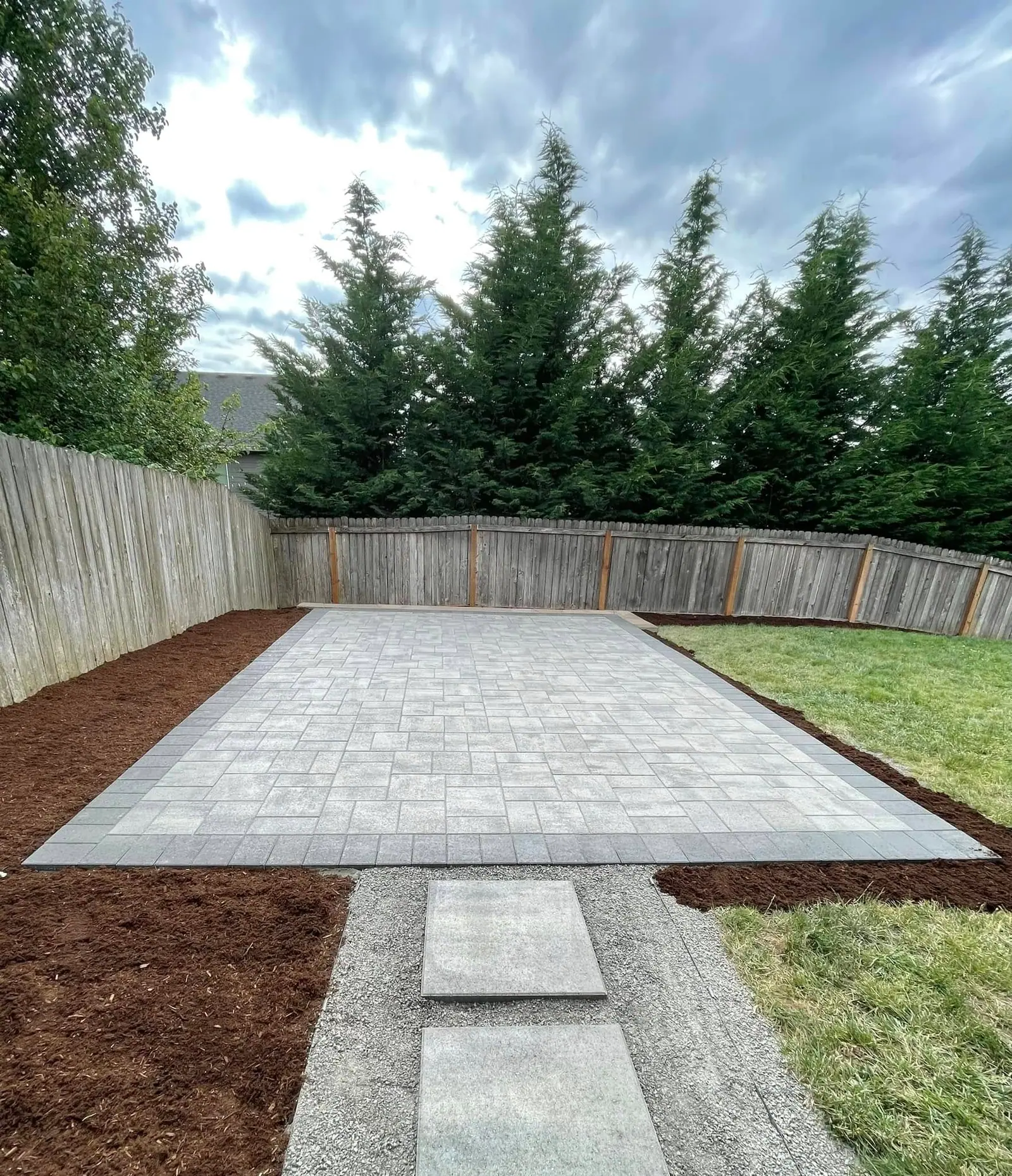 Paver patio with a curved fence line and bark planting bed