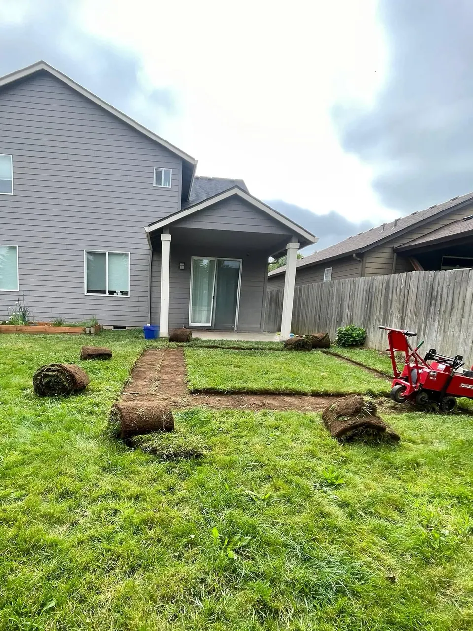 Sod rolls being unrolled and seamed across a prepared backyard